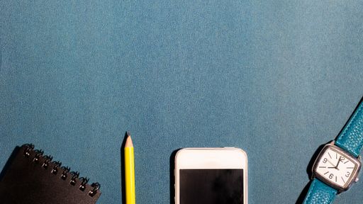A pencil, smartphone, watch and a small notebook on a blue surface