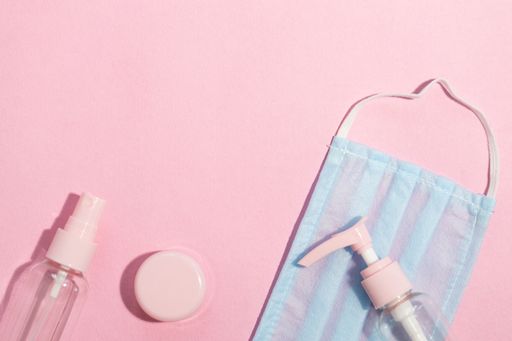 A closeup shot of a hand sanitizers and protective face masks on a pink background
