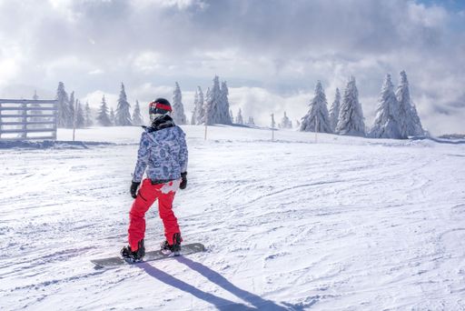 A snowboarder riding down the hill in a mountain ski resort with fir trees in the background