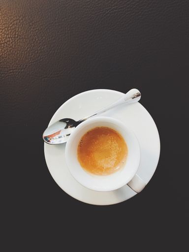 A vertical high angle shot of a cup of coffee and a spoon on a black surface