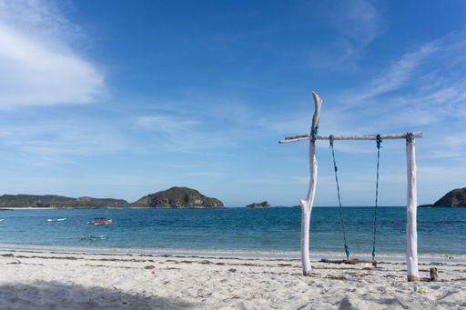 A empty wooden swing on the seashore with a view of the horizon and rocks