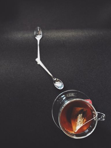 A vertical high angle shot of a cup of tea and two spoons arranged like a watch - time management concept