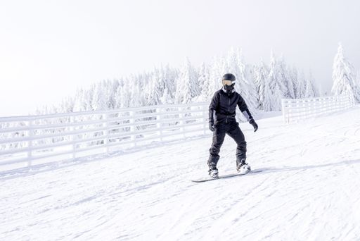 A snowboarder in motion riding down the hill in the mountain resort