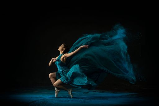 An emotional Southeast Asian ballet dancer in a green dress with powder performing a move on a black background