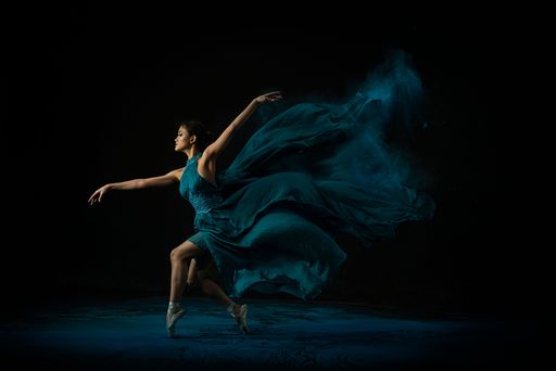 An emotional Southeast Asian ballet dancer in a green dress with powder performing a move on a black background