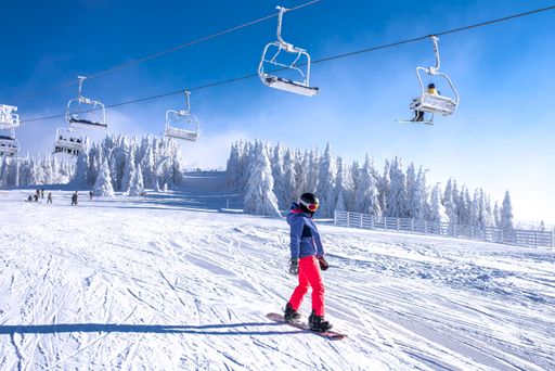 A snowboarder riding down the hill in the mountain resort with cable cars in the background