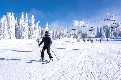 A skier sliding down the hill with ski lift in the background
