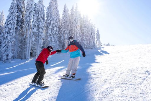 Two snowboarders holding hands while riding down the hill