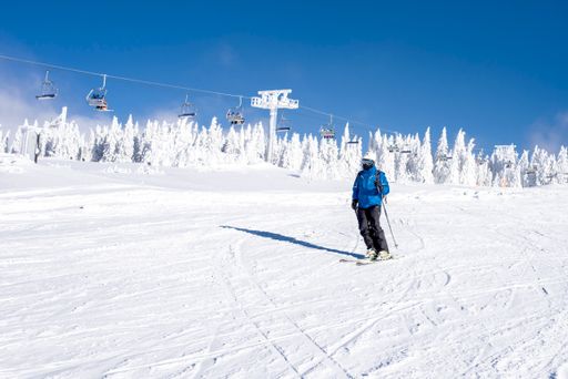 A skier riding down the hill in the mountain resort with cable cars in the background