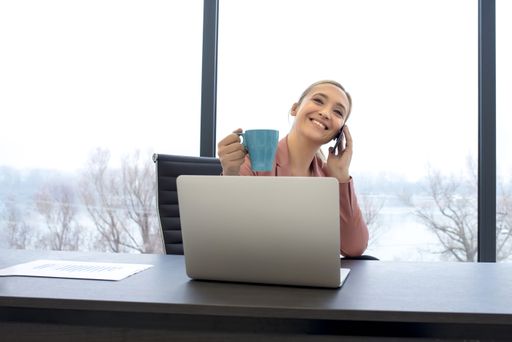 A young female talking on her phone and drinking coffee at the office