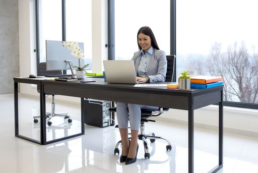 A young businesswoman working on a laptop in her modern office with glass walls