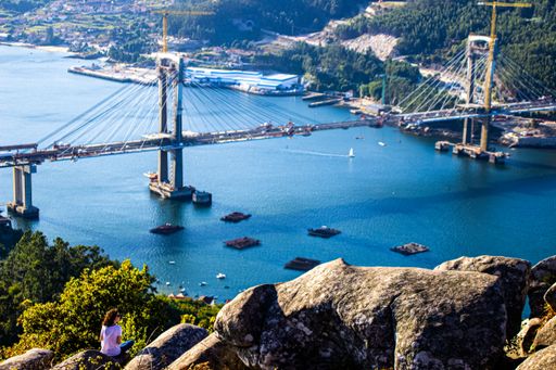 A girl on a hillside admires the beautiful view of the Rande bridge and the estuary in Vigo, Galicia