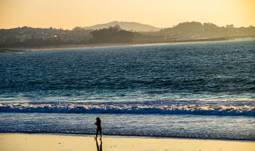 A girl walks on a sandy beach by the river with a view of the Rande bridge and the estuary in Vigo, Galicia