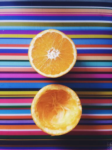 A high angle vertical shot of a sliced orange and an empty orange peel on a colorful striped surface