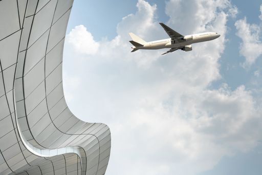 airplane fly in sky with edge of modern building and empty cloudy sky