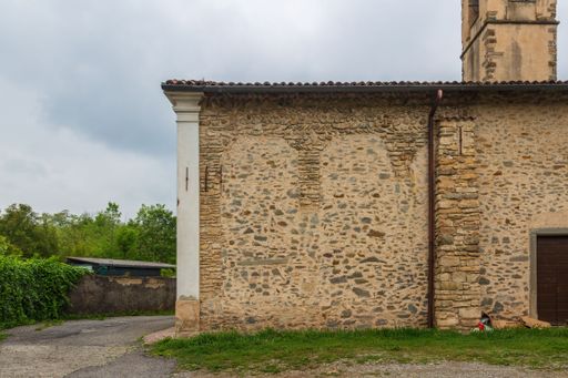 The walls of the church of San Donato with trees in the yard under a cloudy sky in Terno d'Isola