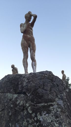 A vertical shot of a human shaped stone statue covered in moss - thinking minds