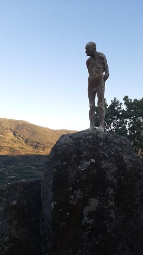 A vertical shot of a human shaped stone statue covered in moss - thinking minds