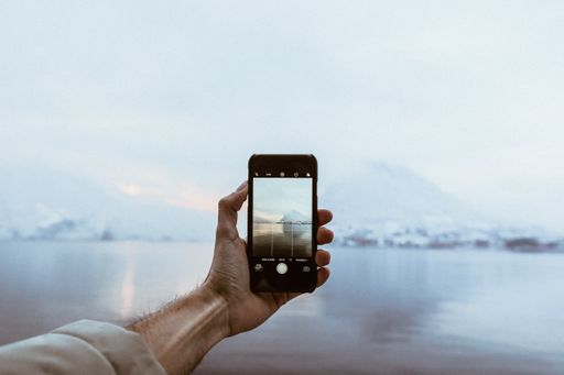 A closeup shot of a person with a smartphone taking a picture of beautiful mountains near the lake enveloped in fog