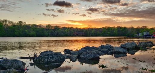 An aerial view of lake surrounded by growing lush green trees in Griggs reservoir park during sunset