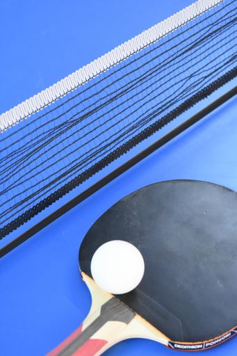 A closeup shot of a table tennis racket with a ball and a net next to it on a blue surface