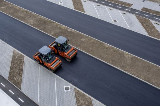 An aerial view of orange vibratory asphalt roller compactor on a new pavement