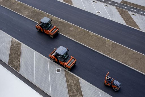An aerial view of orange vibratory asphalt roller compactor on a new pavement