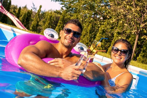 A closeup shot of a young couple drinking cocktails and smiling in a pool