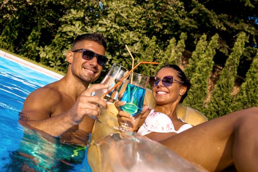 A low angle shot of a smiling couple holding cocktails in the swimming pool