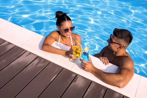 A high angle shot of a smiling group of a couple holding cocktails in the swimming pool
