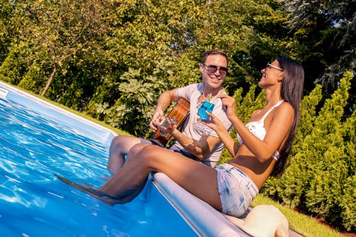 A high angle shot of a smiling couple holding cocktails a guitar in the swimming pool