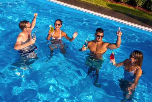 A group of young friends holding cocktails and having fun in a pool on a sunny day
