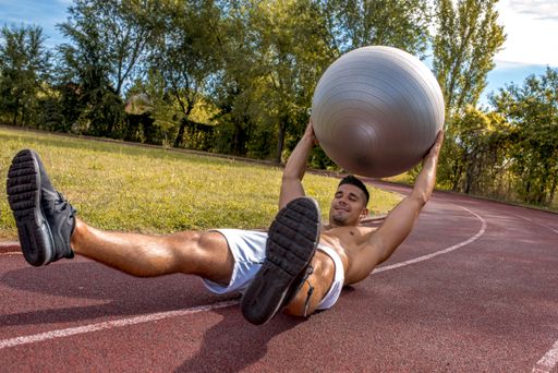 A young shirtless Caucasian male working out in the park at daytime