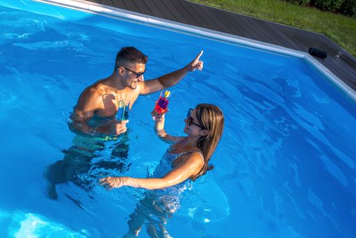 A high angle shot of a smiling couple holding cocktails in the swimming pool