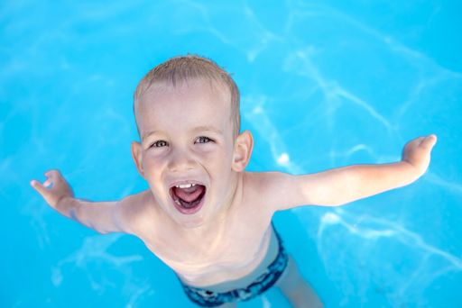 A Caucasian young boy swimming in the pool and happily smiling
