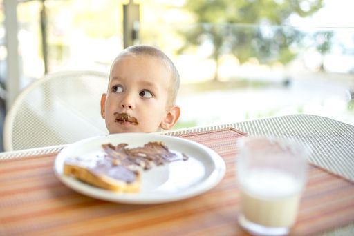 A male child with chocolate on his mouth with a plate of bread with hazelnut spread in front of him