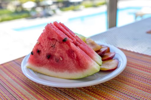 A closeup shot of sliced watermelon and plums in a plastic plate
