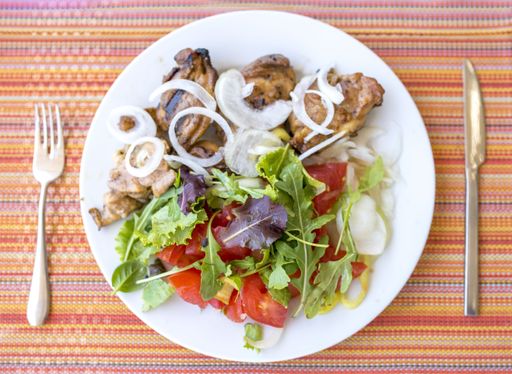 An overhead shot of a plate with meat and vegetables with a fork and knife on a striped tablecloth