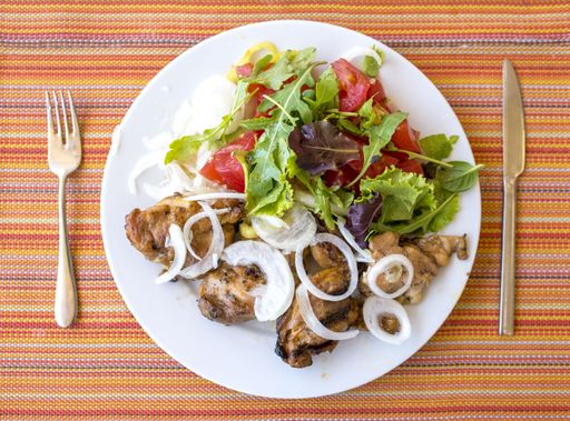 An overhead shot of a plate with meat and vegetables with a fork and knife on a striped tablecloth