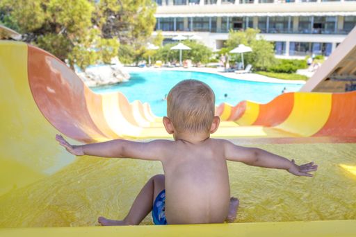 A high angle shot of a male child going down an orange and yellow slide in the pool