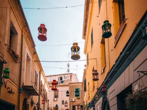A low angle shot of an alley between ancient buildings with colorful lanterns hanging from the cables