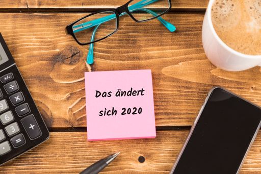 A desk with 'Das andert sich 2020' text on pink paper surrounded by calculator, smartphone and glasses