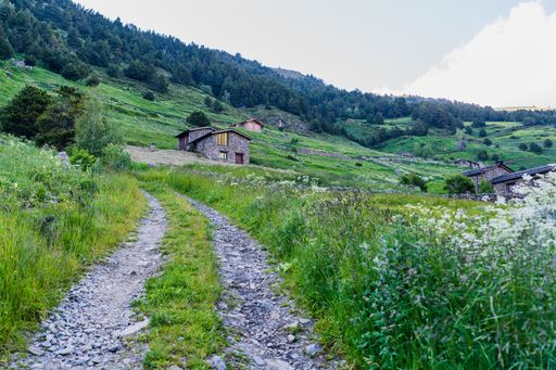 A beautiful shot of a rough rural road on the background of some houses on a green mountain slope