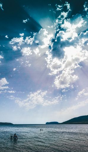 A vertical shot of people swimming in the sea under the bright beautiful sky