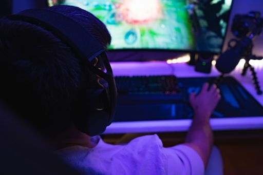 A selective focus of a man in headphones playing a game on a PC in a room with blue light