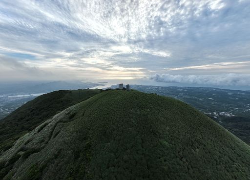 A bird's eye view of a viewpoint on a mountain surrounded by green plants and trees against blue cloudy sky on a beautiful sunny day