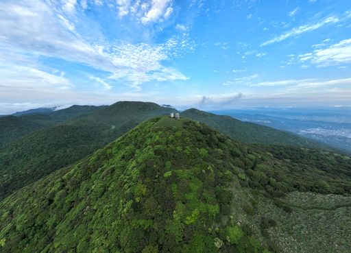 A bird's eye view of a viewpoint on a mountain surrounded by green plants and trees against blue cloudy sky on a beautiful sunny day