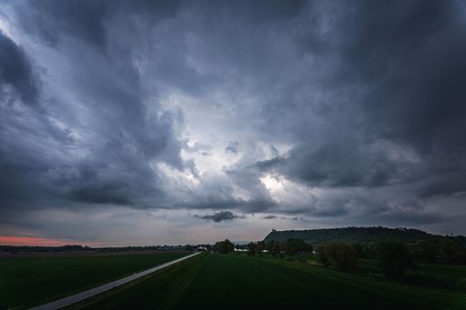 A road surrounded by green fields and trees against dark stormy clouds in Bavaria, Germany