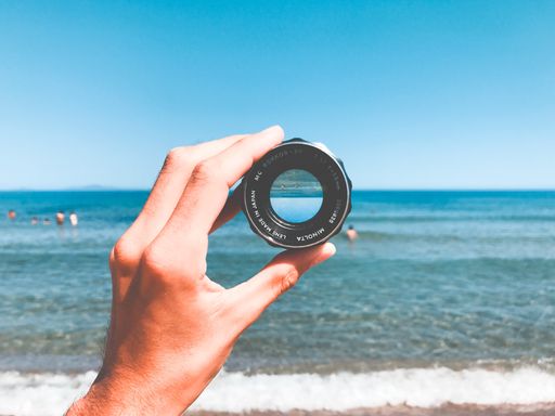 A person holding a lens with the beautiful sea in the background under the calm sky