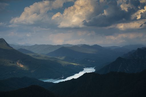 An aerial shot of a river among mountains under cloudy sky